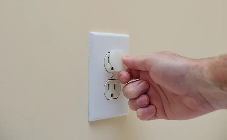 person baby proofing an electrical outlet with a plastic cover