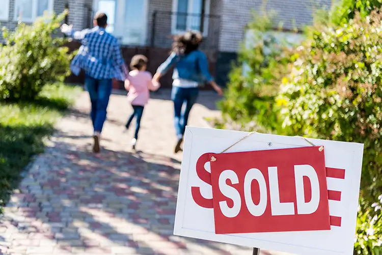 Family towards new house. SOLD stickered on top of Sale sign in the front lawn.